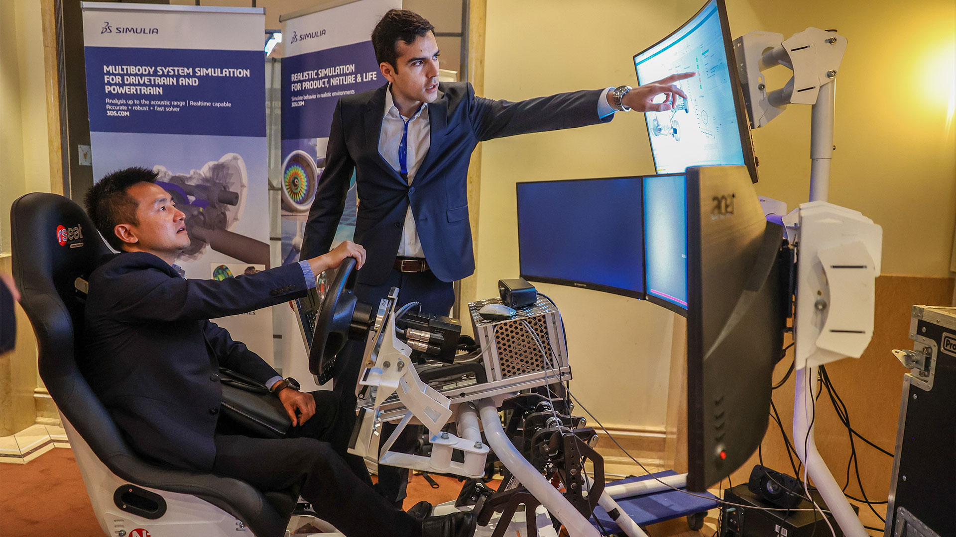 Mann sitzend in einem Fahrsimulator im Ausstellungsbereich bekommt Produkt erklärt. 