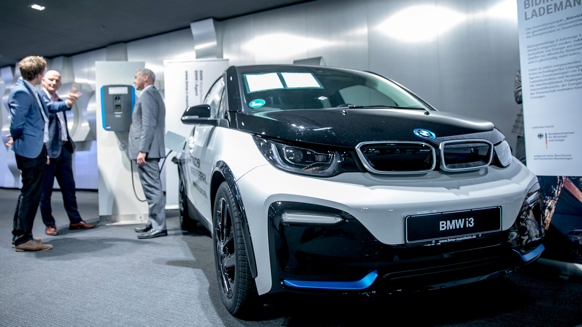 Ausstellungsfahrzeug elektrisch. In Hintergrund drei Herren im Gespräch. 